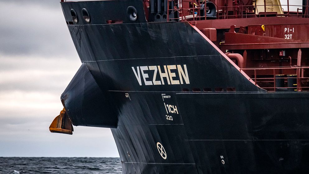 Fartyget ”Vezhen” skär genom vattnet med en tydligt synlig för och ankare, under en mulen himmel.
