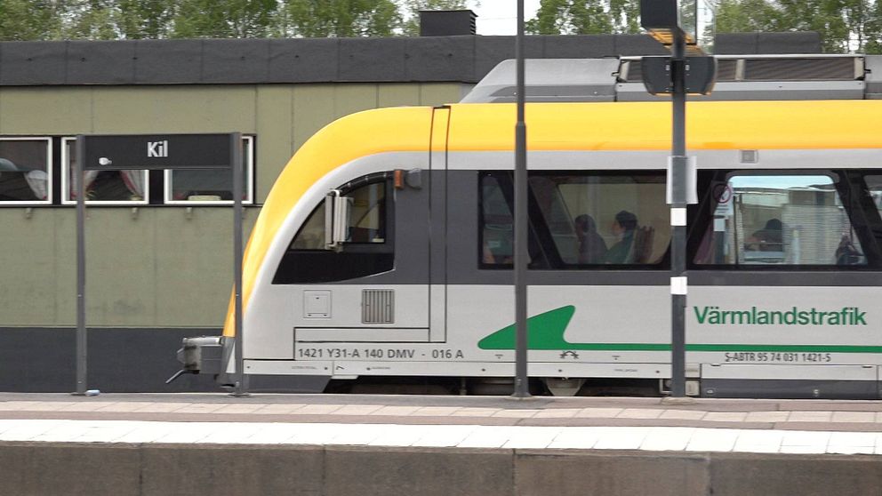 Tåg från Värmlandstrafik vid stationen Kil. I bakgrunden syns en byggnad som tillhör stationen, med en skylt som visar stationens namn. Tåget är delvis synligt, vilket ger en känsla av rörelse och transport.