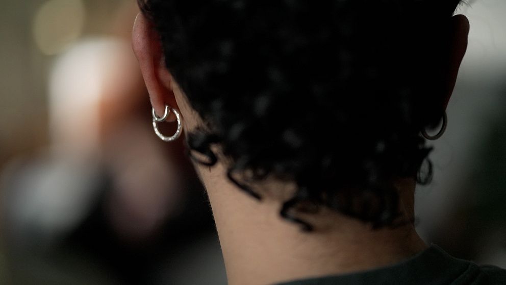Närbild av en persons bakhuvud med lockigt hår och två små örhängen i vänstra örat.