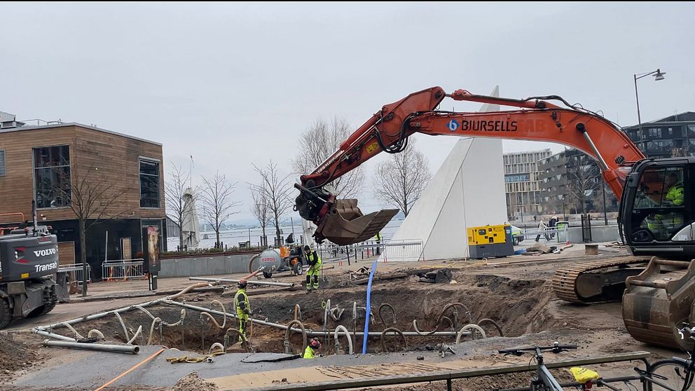 Grävmaskin arbetar på byggarbetsplats nära modern byggnad.