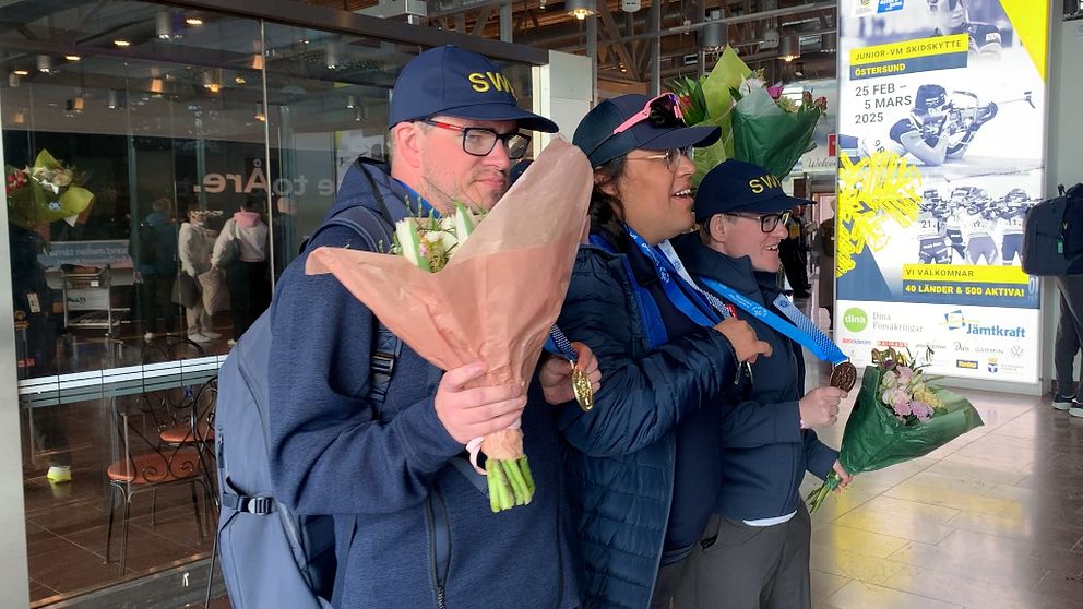 Fyra personer i uniformer håller blombuketter och medaljer vid ett evenemang.