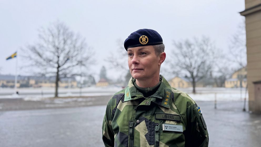 Soldat i uniform står utomhus på en regnig dag med svenskt landskap i bakgrunden.