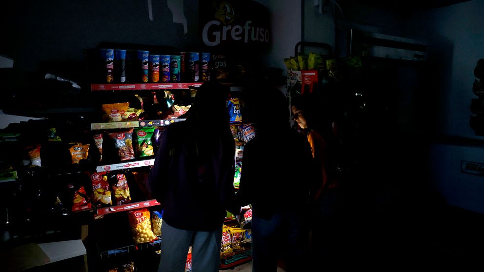 Två personer plockar varor i en mörklagd butik, endast hyllorna är svagt belysta.
