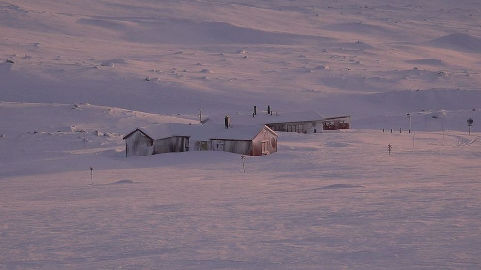 Snötäckt landskap med ett ensamt hus i skymningsljus.