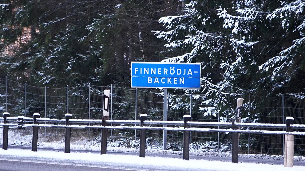 Skylt som visar namnet ”Finnerödja-Backen” vid en snöig väg nära en tät skog.