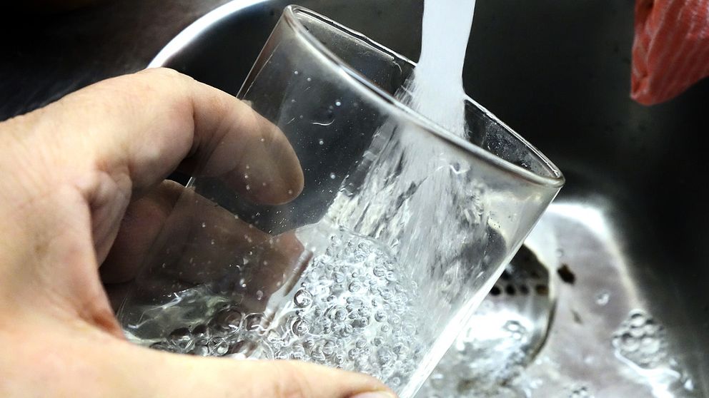 Ett glas som fylls med vatten från vattenkran.