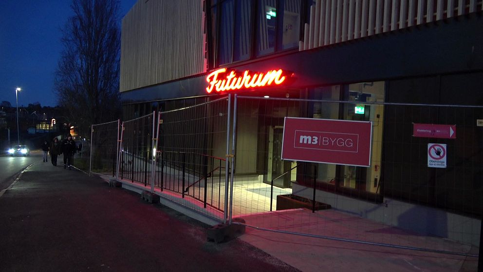 Det är kväll och den gamla neonskylten som lyser gult/orange Futurum i skrivstil. Byggnaden är omgiven av ett byggstaket