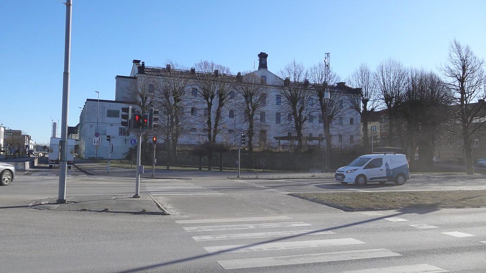 Gatukorsning med en vit skåpbil framför en stor byggnad och träd utan löv.