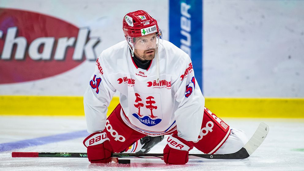 Hockeyspelare i vit och röd dräkt stretchar på isen.