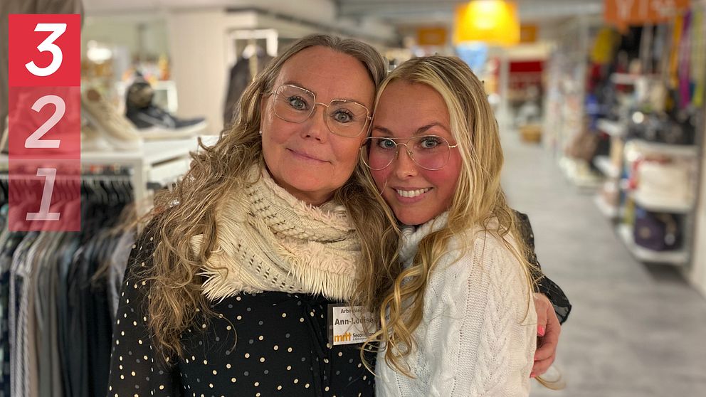 Två personer omfamnade i en butik med kläder i bakgrunden.