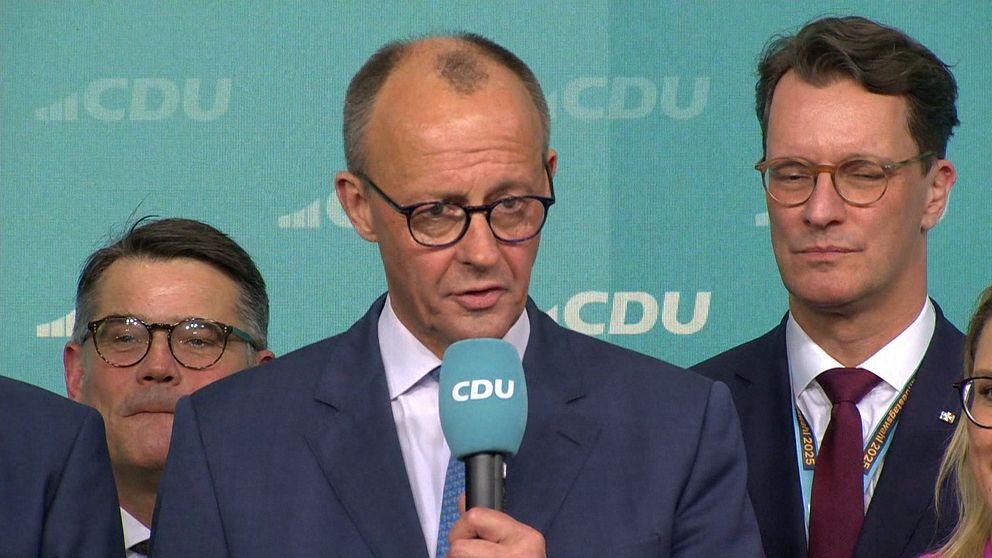 Tunnhårig medelålders man i glasögon och mörkblå kostym talar i CDU-mikrofon framför CDU-bakgrund.