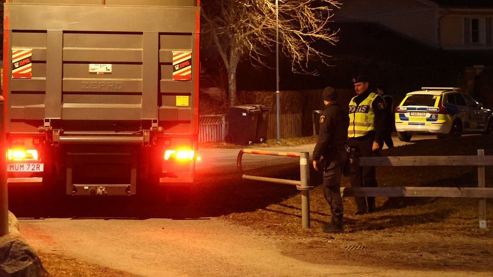 Lastbil med röda ljus. Polis står nära. Hus syns i bakgrunden.