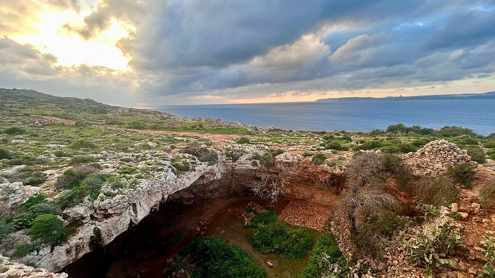 Utsikt över kustlandskap på Malta  med grotta, vegetation och hav under molnigt himmel.