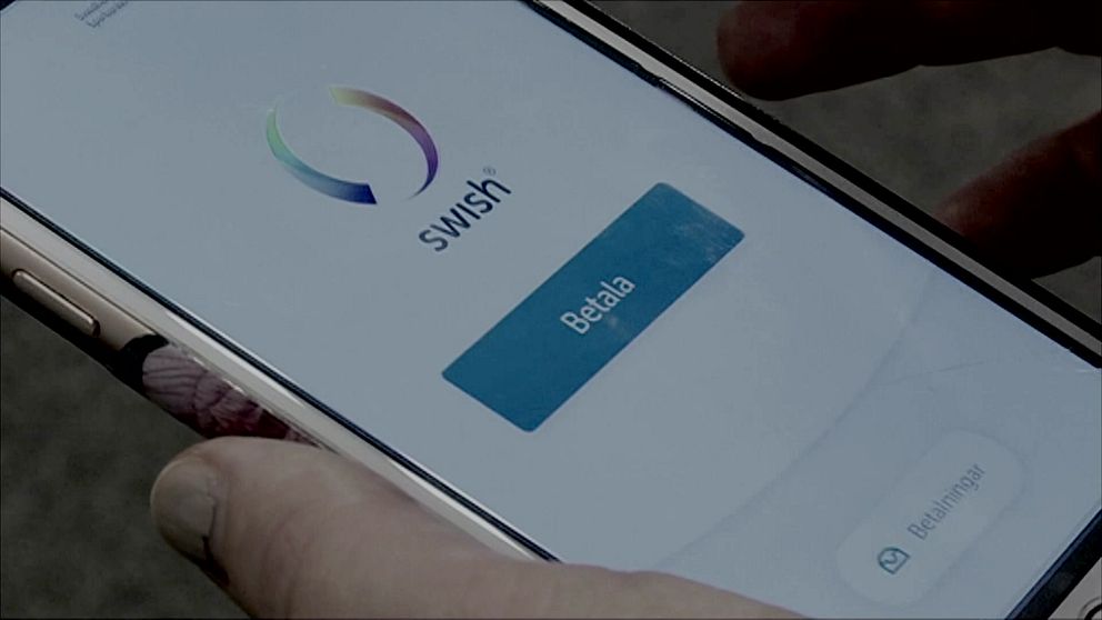 Mobilskärm visar Swish-appen med en knapp för att betala, medan en hand håller telefonen.