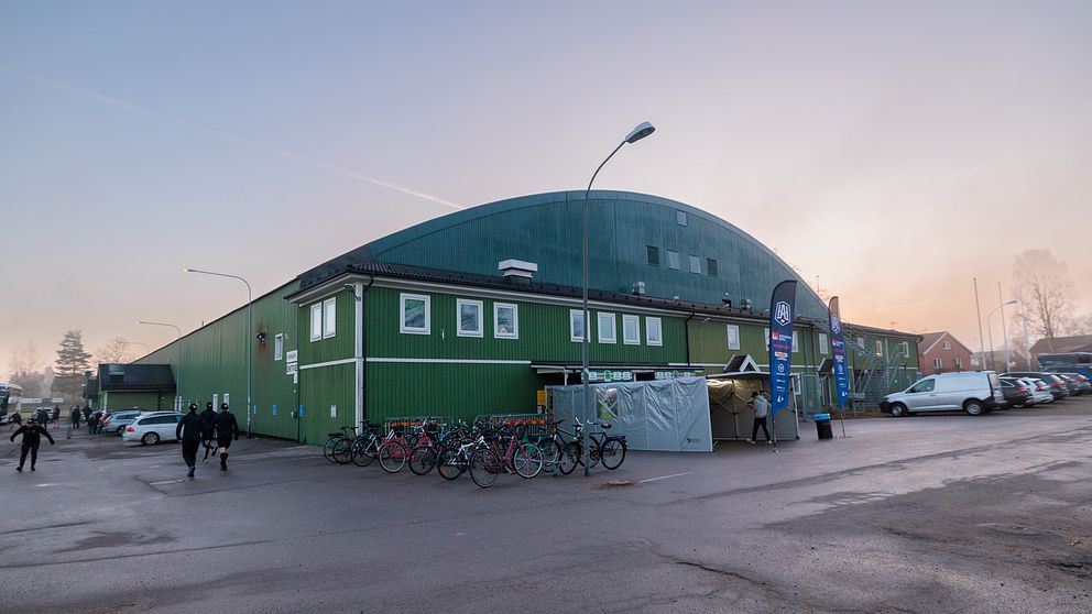Grönt sportkomplex vid solnedgång. Cyklister och gående passerar på vägen.