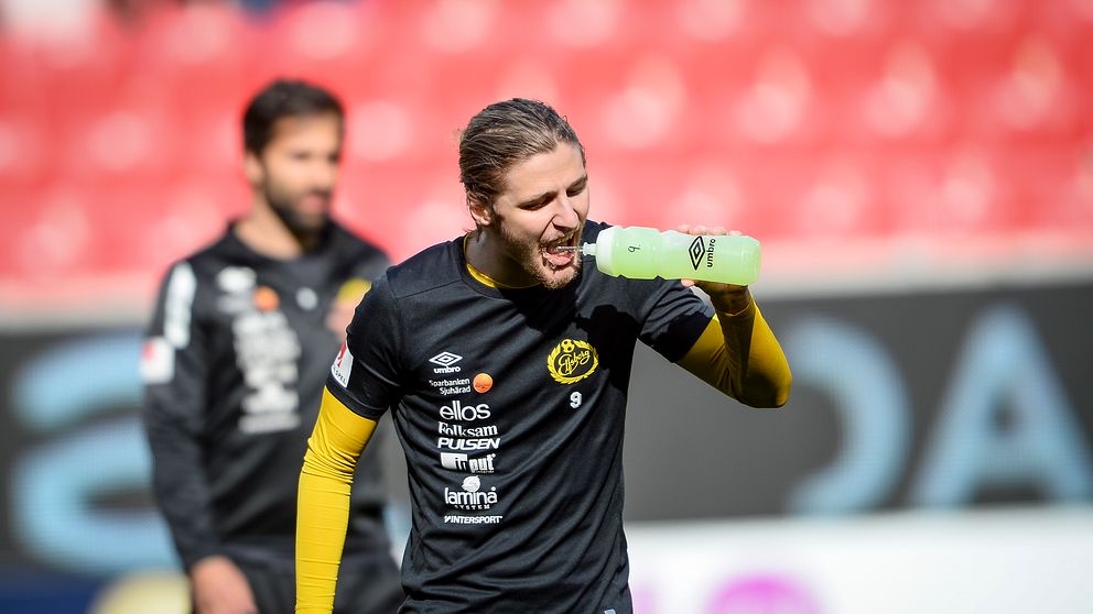 Pawel Cibicki  i svart och gult träningskläder håller en vattenflaska under en match på en stadion, med publik i bakgrunden.