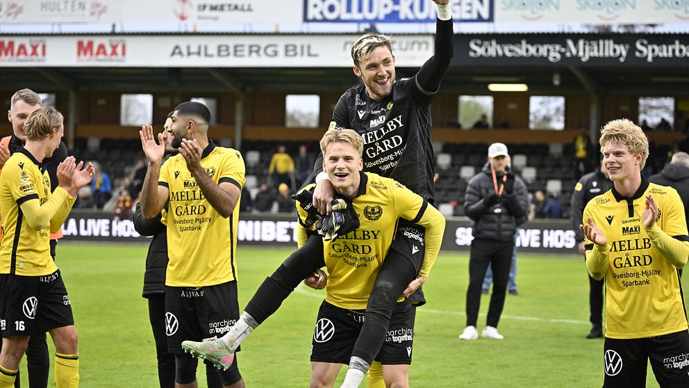 Fotbollsspelare i gula tröjor firar tillsammans på planen efter matchen.