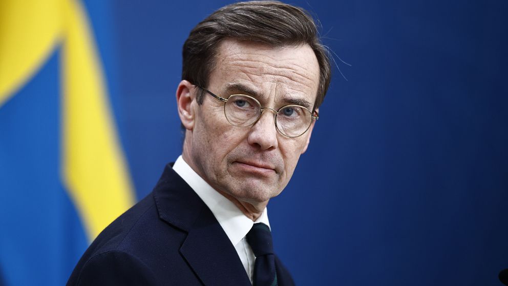 Statsminister Ulf Kristersson i kostym med svensk flagga i bakgrunden.