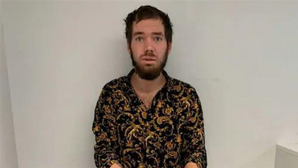 Person med mörkt, mönstrat skjorta står mot en vit vägg.