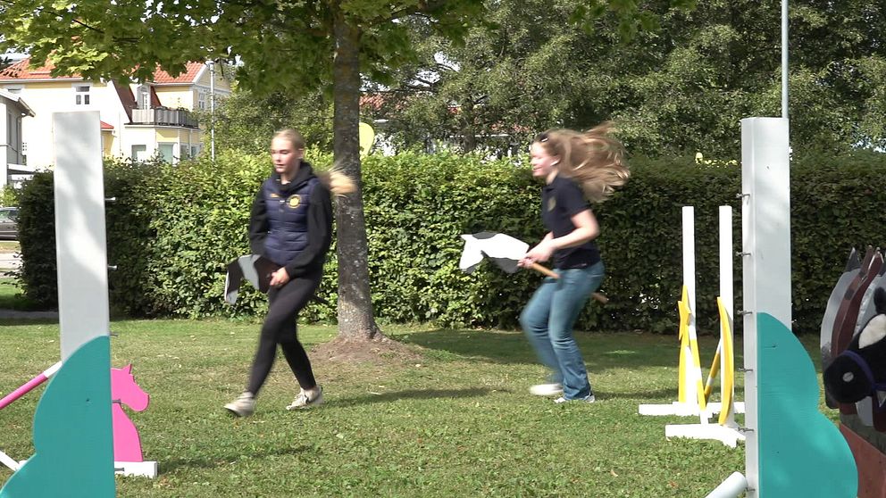 KLara och hennes kompis hoppar käpphäst på en hinderbana.