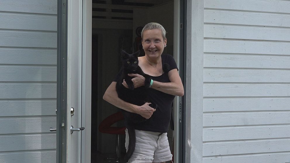 Kvinna håller sin katt i famnen och står i en dörröppning.