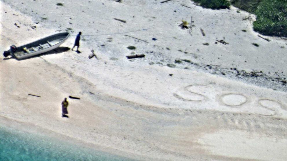 De två männen på stranden, med SOS skrivet i sanden.
