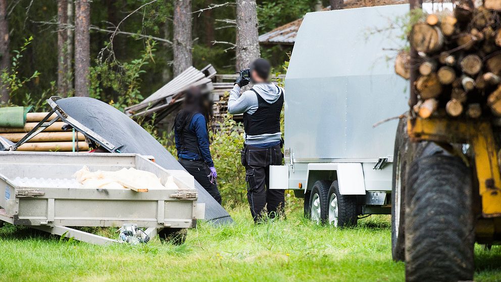 två poliser på en gård, släpvagnar och en traktor syns