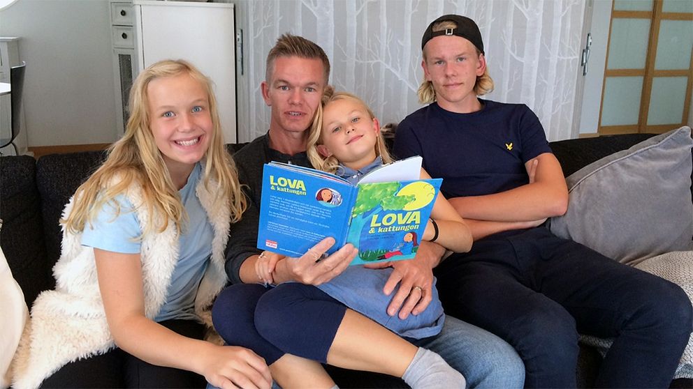 Christian Jeppsson sitter i soffan omgiven av sina tre barn och håller i boken Lova och kattungen