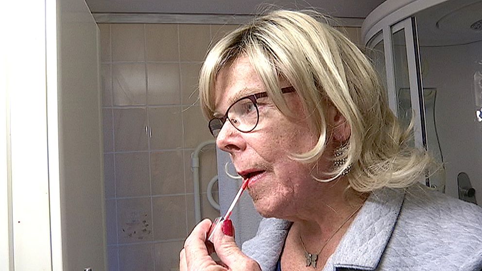 Tina Springer målar läppglans på läpparna. Hon står i sitt badrum.