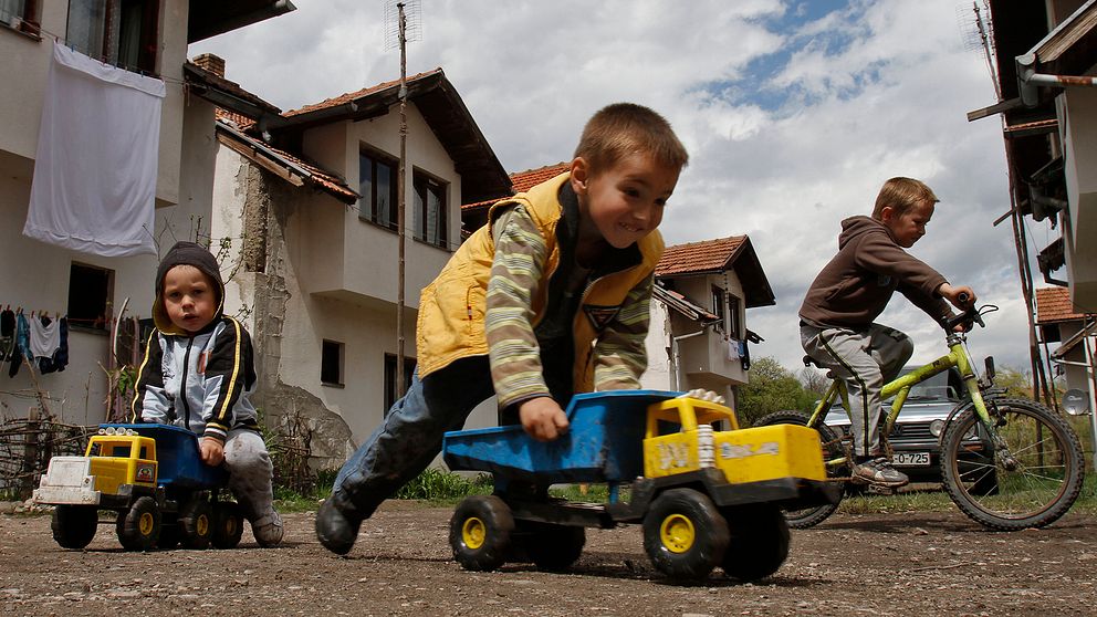 Tre barn leker med lastbilar och en cykel i norra Bosnien.