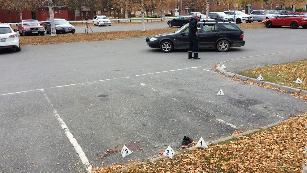 Tekniker undersöker brottsplatsen. En sko och blod syns på parkeringen.