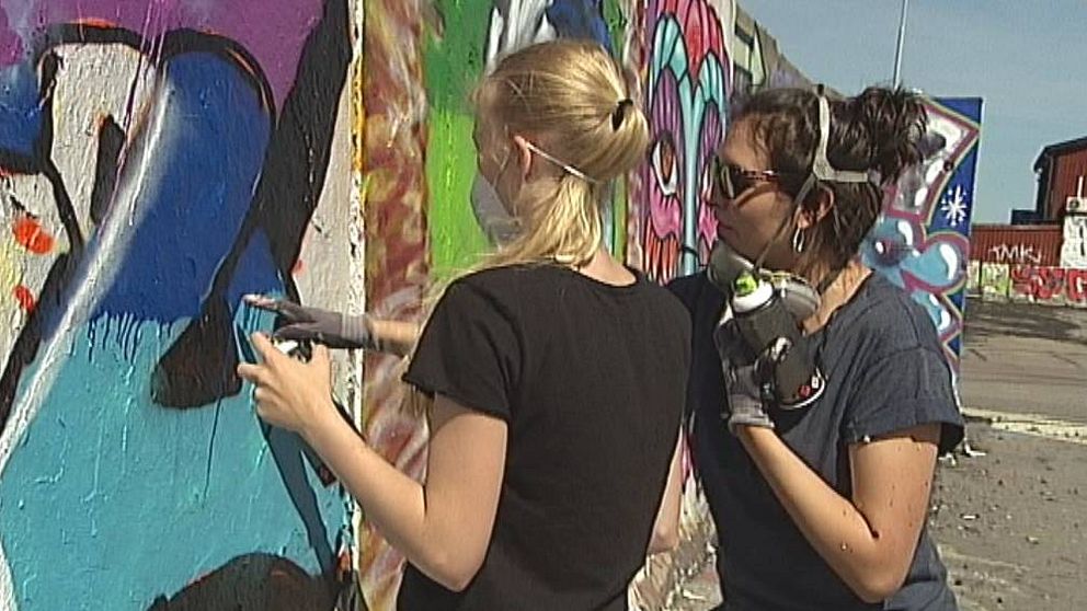 Två graffitimålare framför en graffitivägg