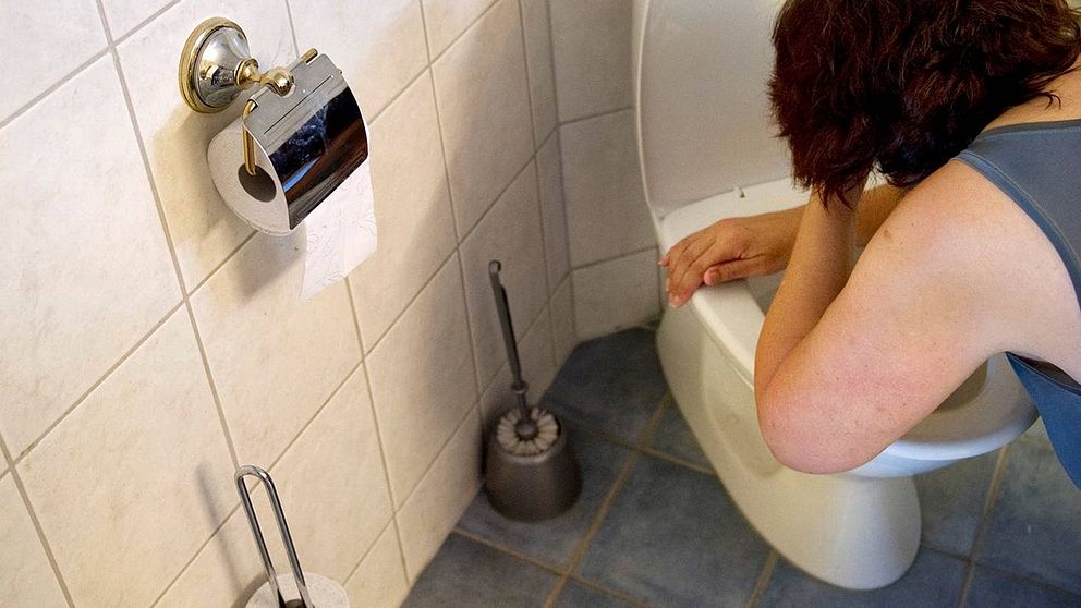 En kvinna står böjd över en toalett.