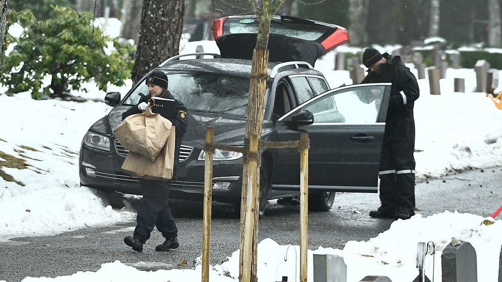 Två poliser utanför en bil, en polis bär på en brun papperspåse.