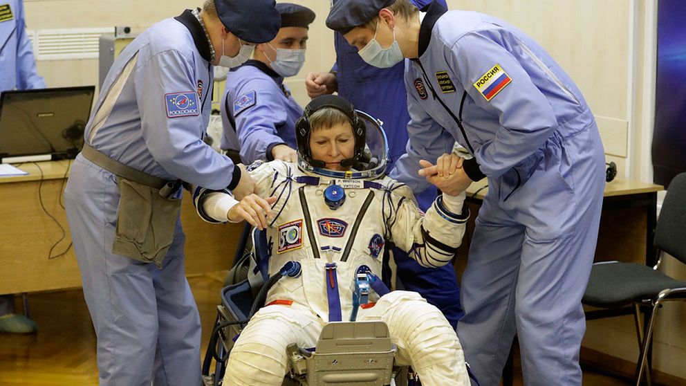 Astronauten Peggy Whitson, en av besättningsmedlemmarna på ISS, får hjälp att resa sig efter att hennes rymddräkt inspekterats före avfärden från Baikonur.