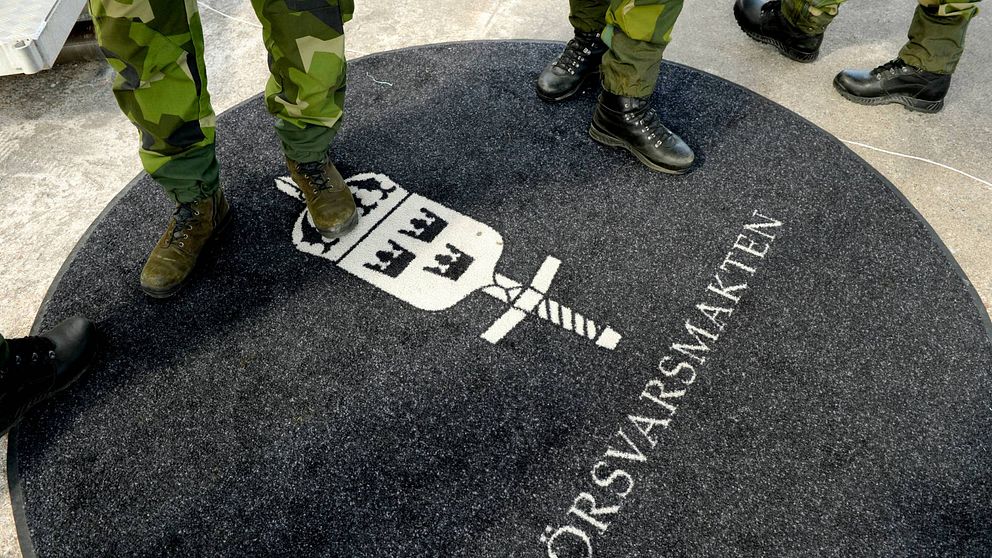Fötter och ben i militära kläder på en matta med texten Försvarsmakten