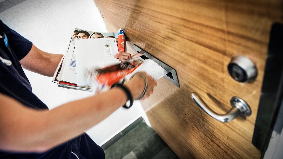 En brevbärare lägger post i ett brevinkast.