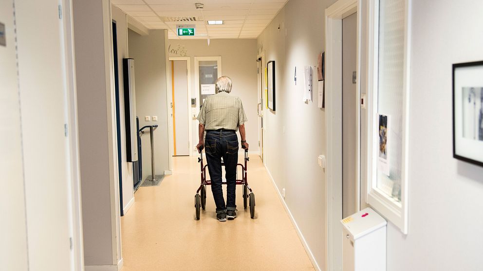 Äldre man går med rullator i en korridor