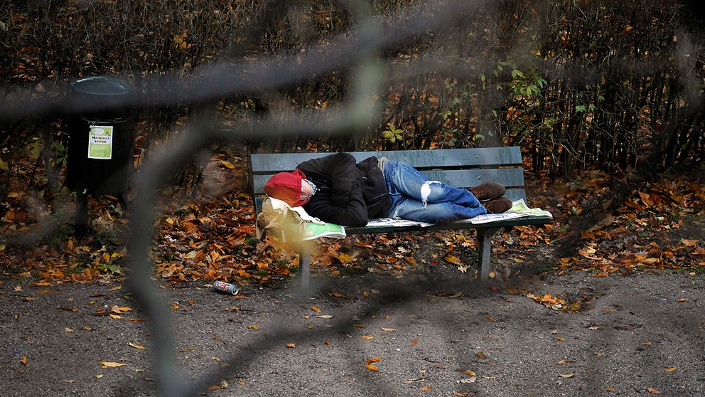 Hemlös person ligger och sover på en parkbänk.