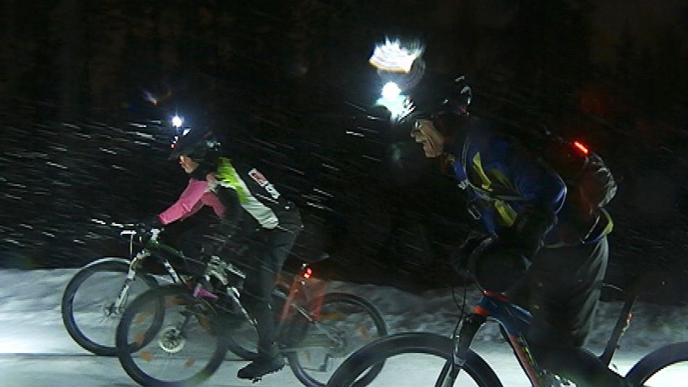 Tre cyklister med pannlampor stretar i ymnigt snöfall