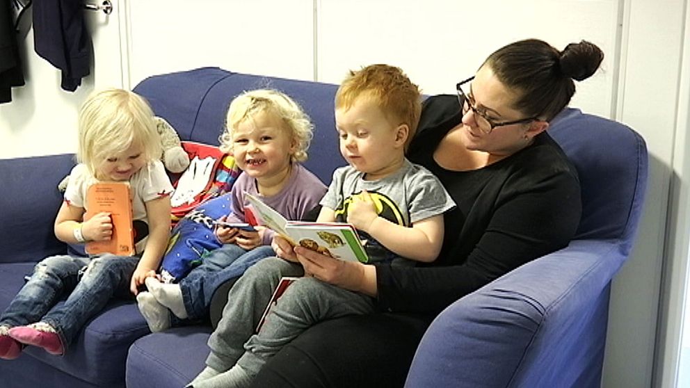 Tre barn sitter tillsammans med sin förskolelärare och läser böcker.