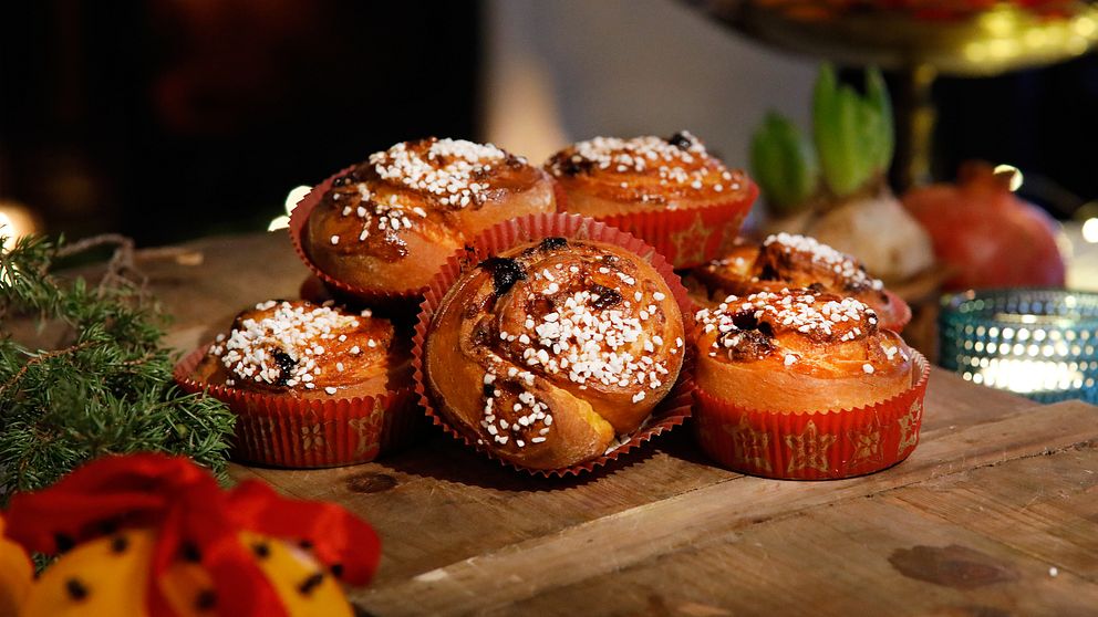 Färdiggräddade bullar dekorerade med pärlsocker i pappersformar ligger på skärbräda av trä.
