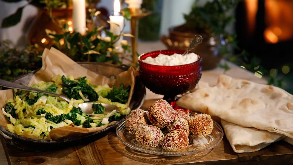 Bollar med rödbetsfalafel på glasfat. Bredvid står röd skål med äppelyoughurt och ett fat med stekt kål, samt libanesiskt bröd.