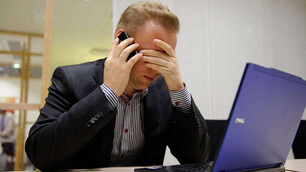 Man pratar i telefon och håller sig för ögonen framför en dator.