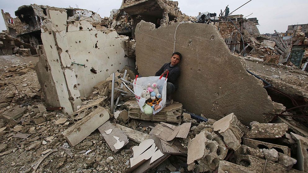 En pojke sitter vid en påse med sina saker som han samlat in bland ruinerna av sitt hus.