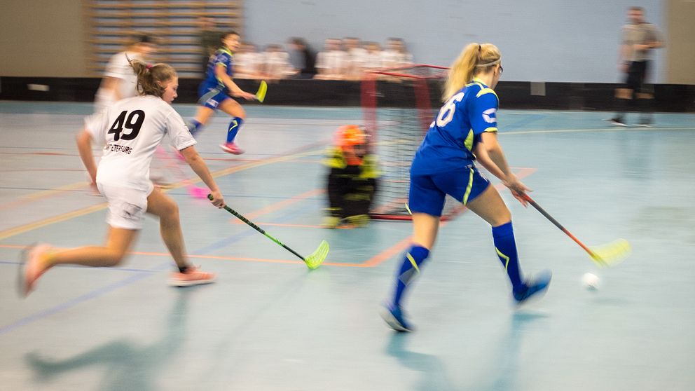 Två innebandyspelare som rör sig runt baksidan av målet.