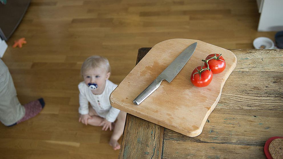 Faror i hemmet för små barn. En bebis riskerar att få tag på en vass kniv hemma i köket.