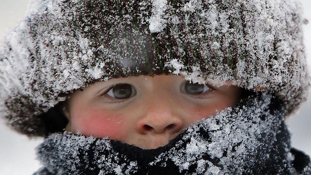 närbild på litet barn med stor mössa och halsduk, snöig