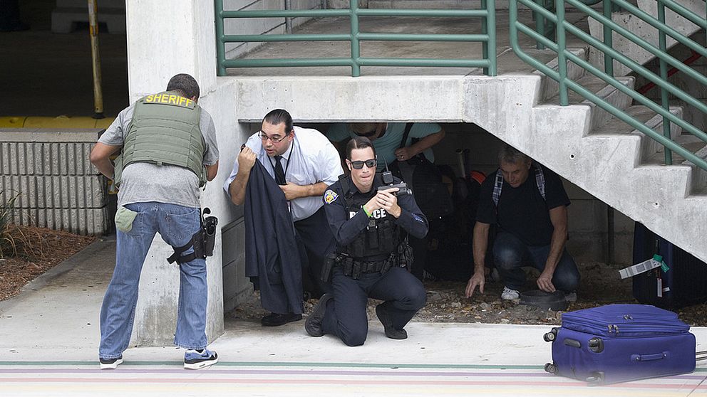 En polis som tar skydd vid en trappa håller i ett vapen.