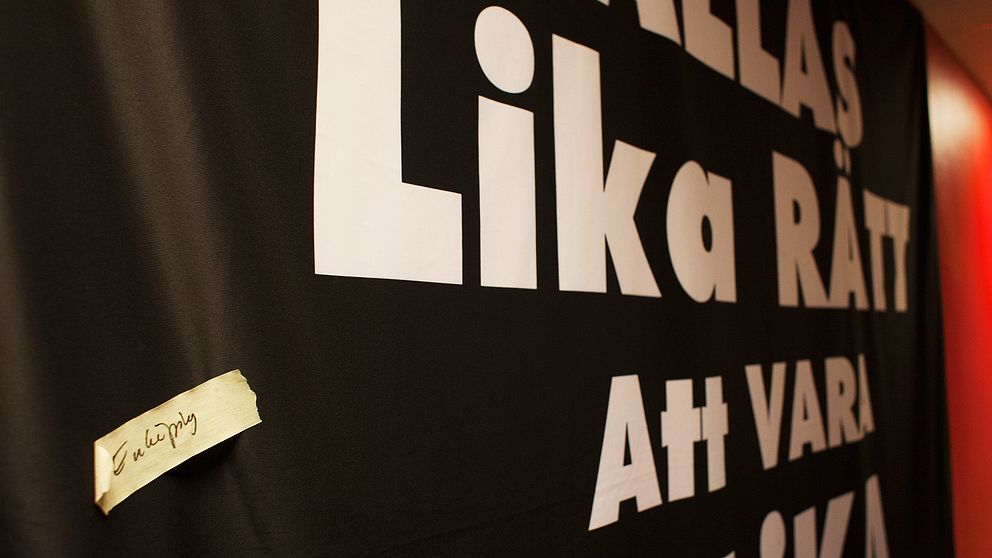 En tejpbit med texten Enköping sitter klistrad på en banderoll. Banderollen har texten ALLAS LIKA RÄTT ATT VARA OLIKA, skriven på sig.
